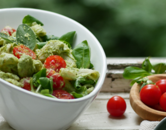 Eine weiße Schale mit Nudelsalat mit Spinat, Tomaten und Avocado-Salbei-Pesto